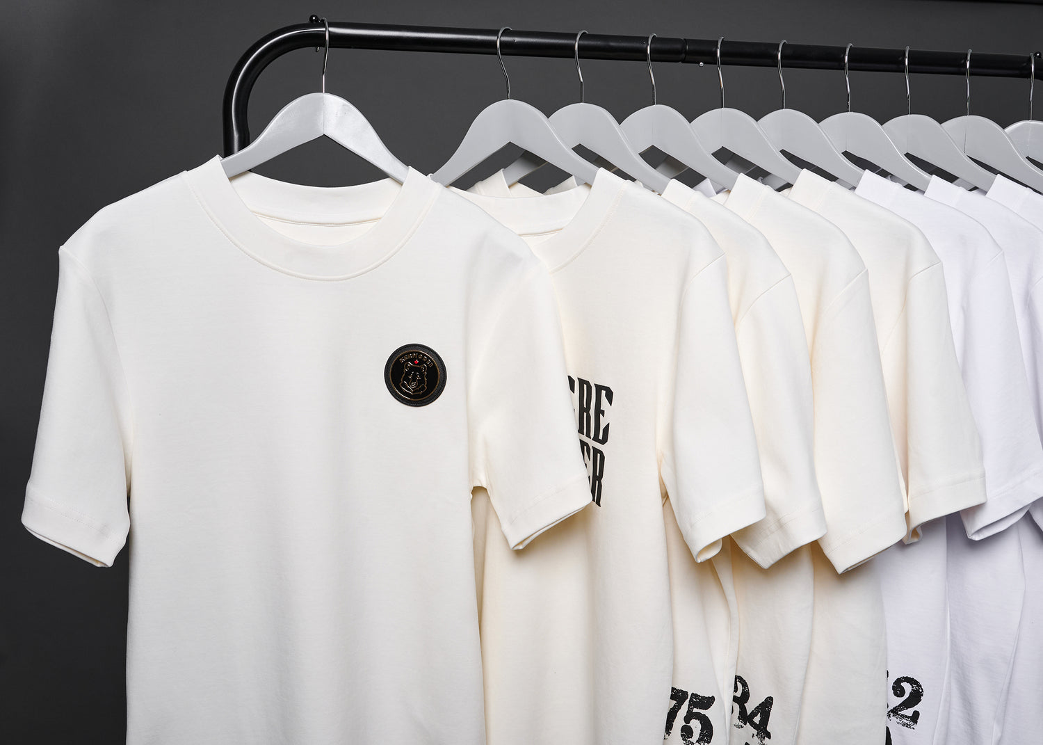 White Kermodee t-shirts on a rack, showcasing gold bear emblem and bold Canadian heritage prints.