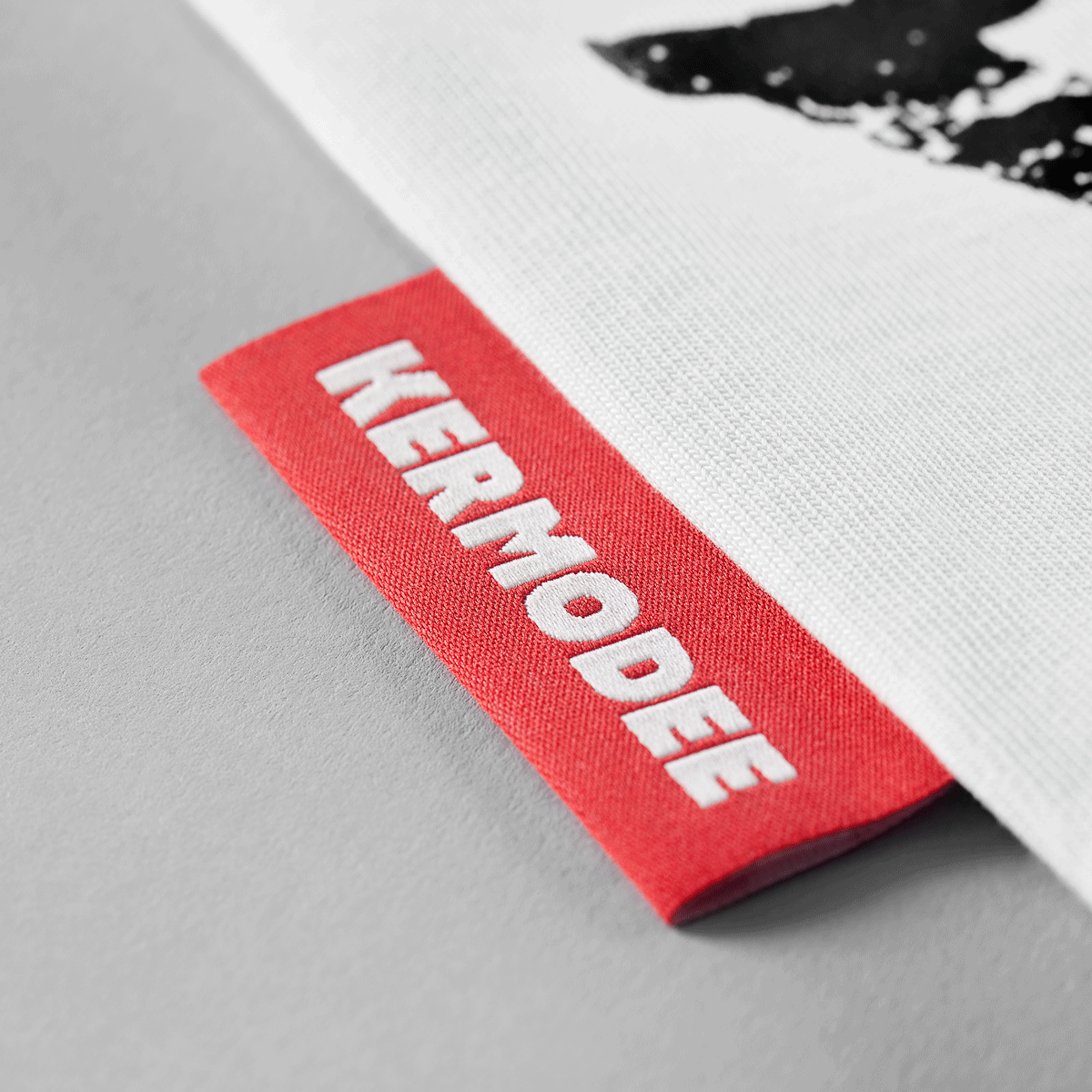 Close-up of red KERMODEE side label on white t-shirt right-side seam