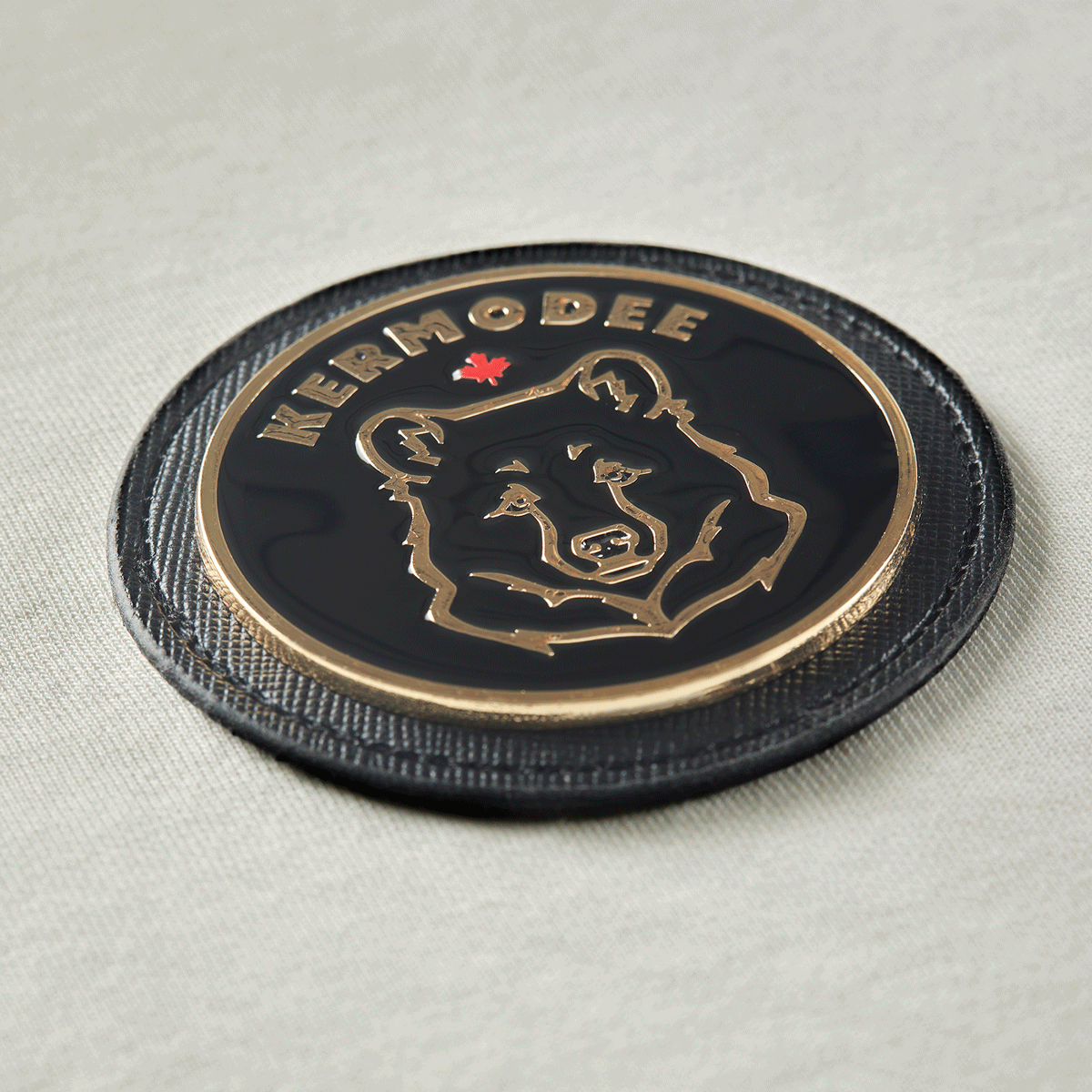 Close-up of circular Kermodee bear emblem with gold contour on cream off-white t-shirt