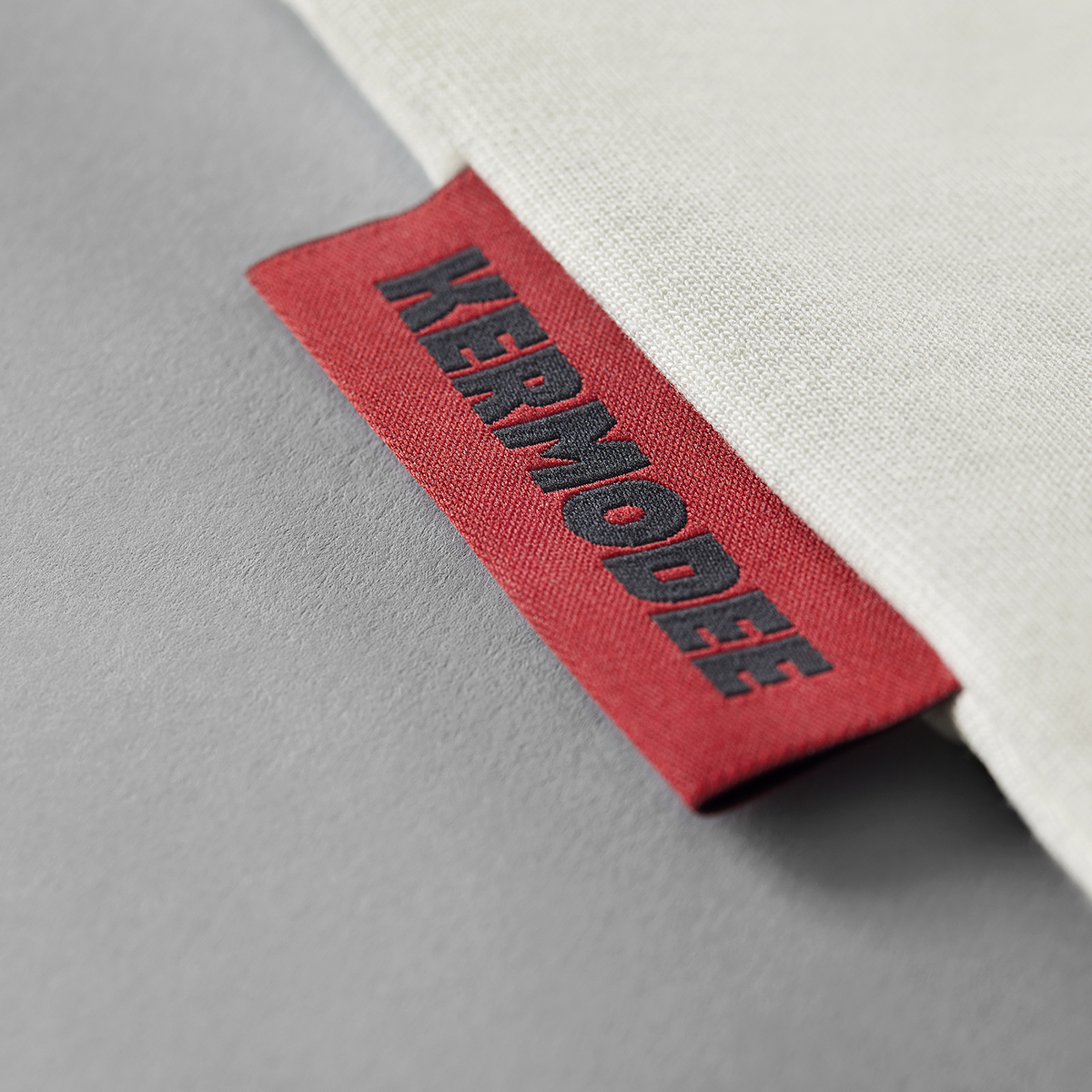 Close-up of red KERMODEE side label on white cream t-shirt seam