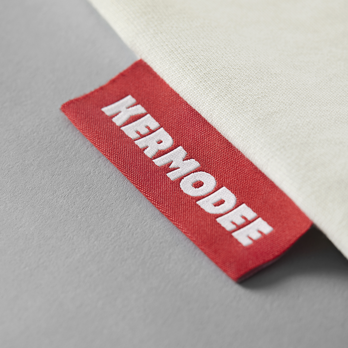Close-up of red KERMODEE side label on white cream t-shirt right-side seam