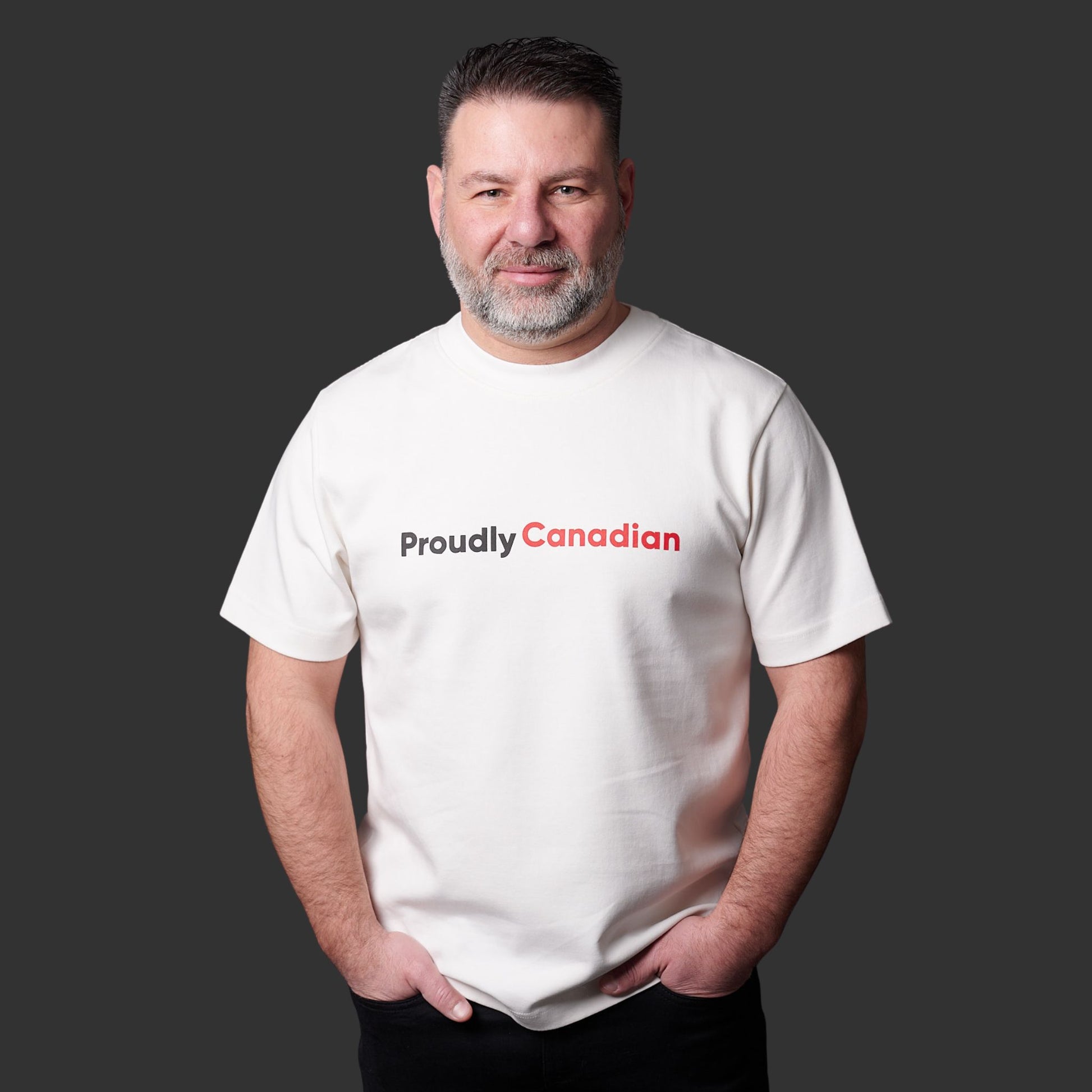 Male model wearing Proudly Canadian Unisex T-Shirt featuring raised high-density red Canadian and black Proudly typography on off-white cotton blend fabric