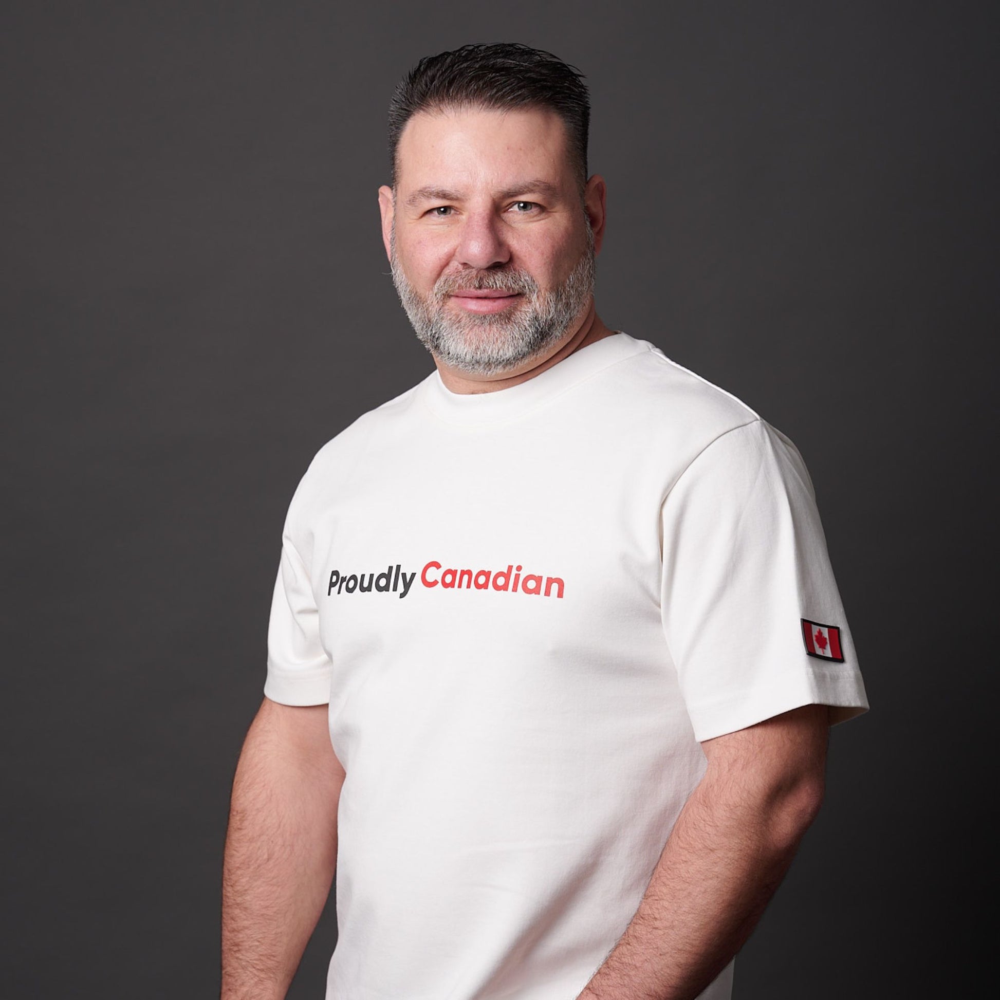 Male model wearing Proudly Canadian Unisex T-Shirt featuring raised high-density red Canadian and black Proudly typography on off-white cotton blend fabric