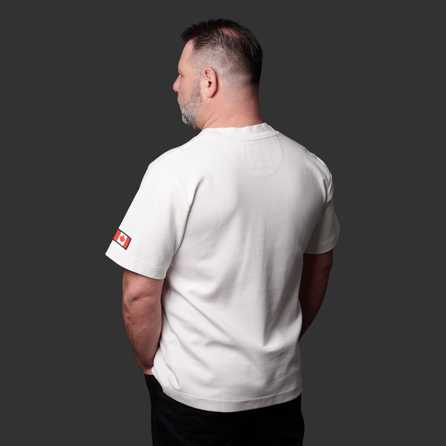 Close-up of Canadian flag silicone patch on left sleeve of Proudly Canadian Unisex T-Shirt made of off-white cream premium cotton blend