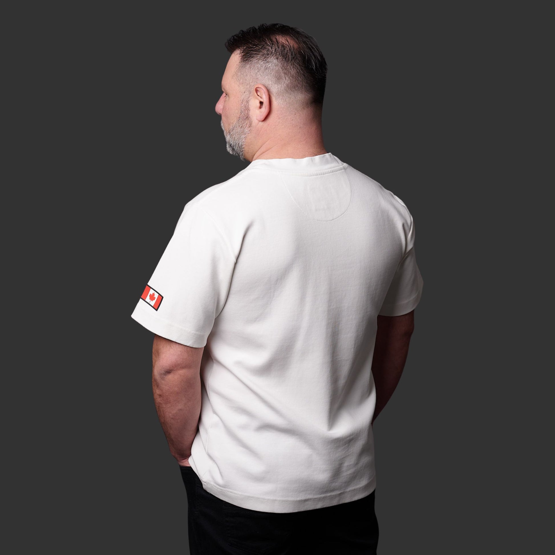 Close-up of Canadian flag silicone patch on left sleeve of Proudly Canadian Unisex T-Shirt made of off-white cream premium cotton blend