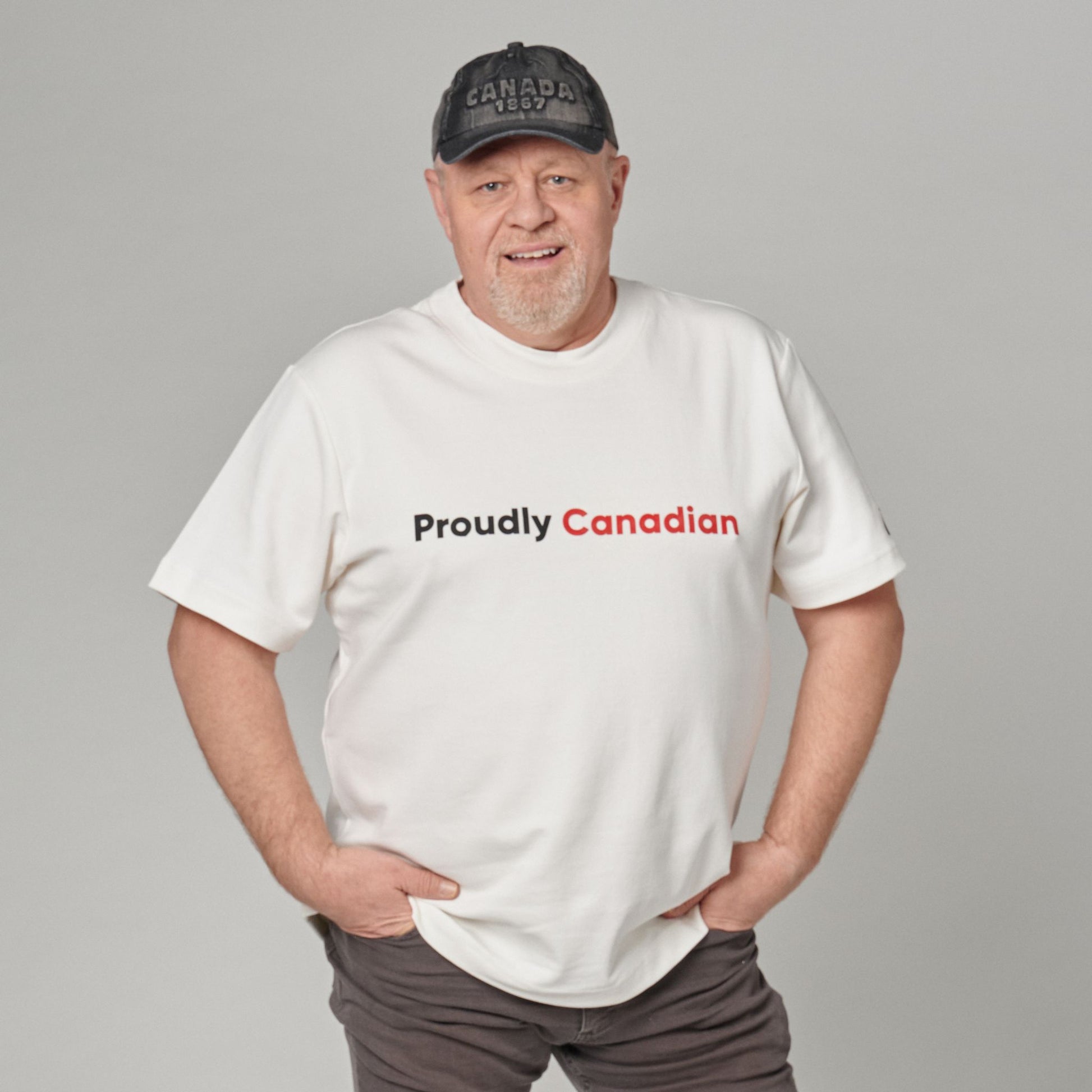 Male model wearing Proudly Canadian Unisex T-Shirt featuring raised high-density red Canadian and black Proudly typography on off-white cotton blend fabric