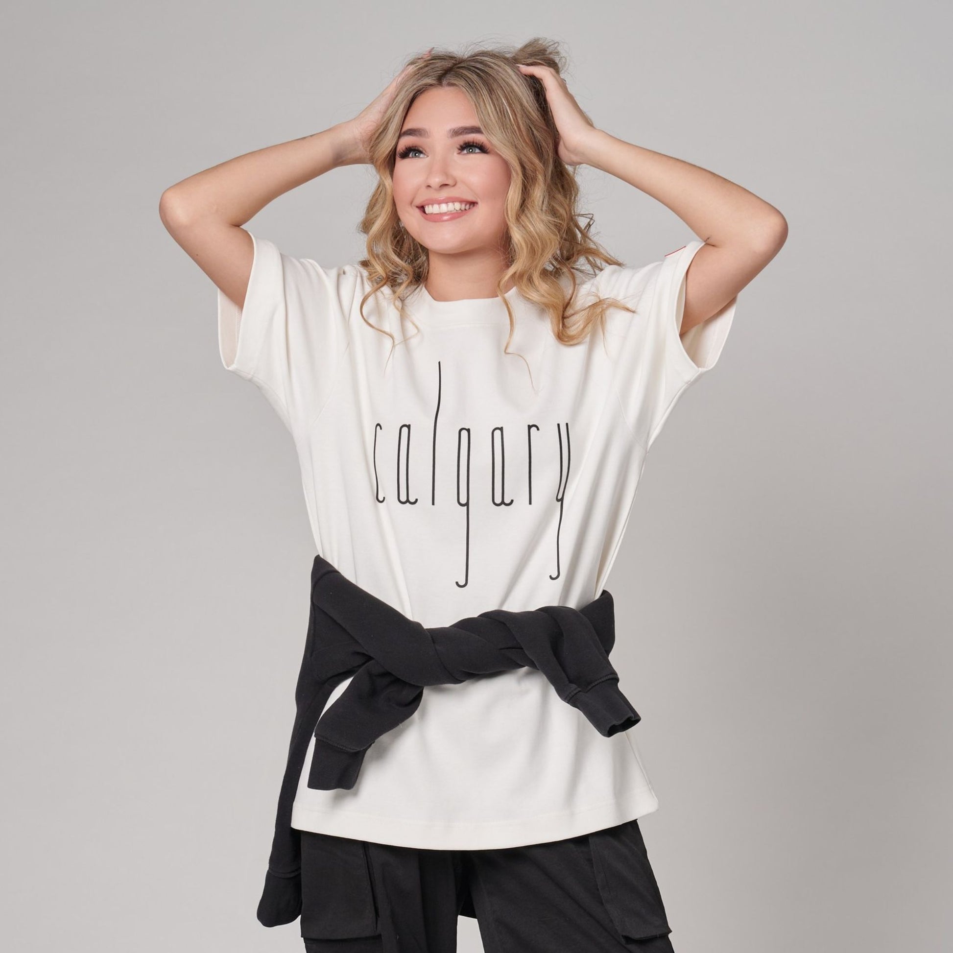 Female model wearing Calgary Alberta Unisex T-Shirt featuring raised high-density Calgary typography on premium off-white fabric