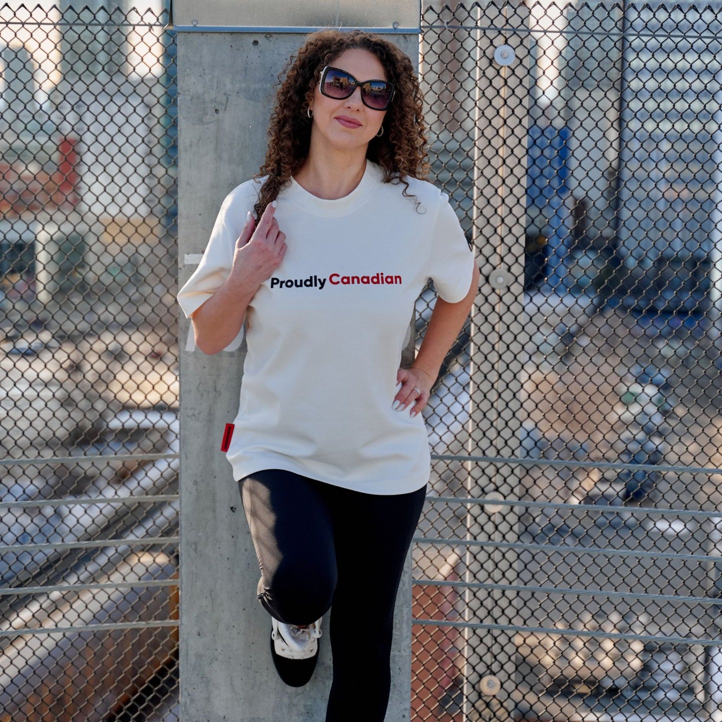 Female model wearing Proudly Canadian Unisex T-Shirt with raised high-density red Canadian and black Proudly typography on premium off-white fabric