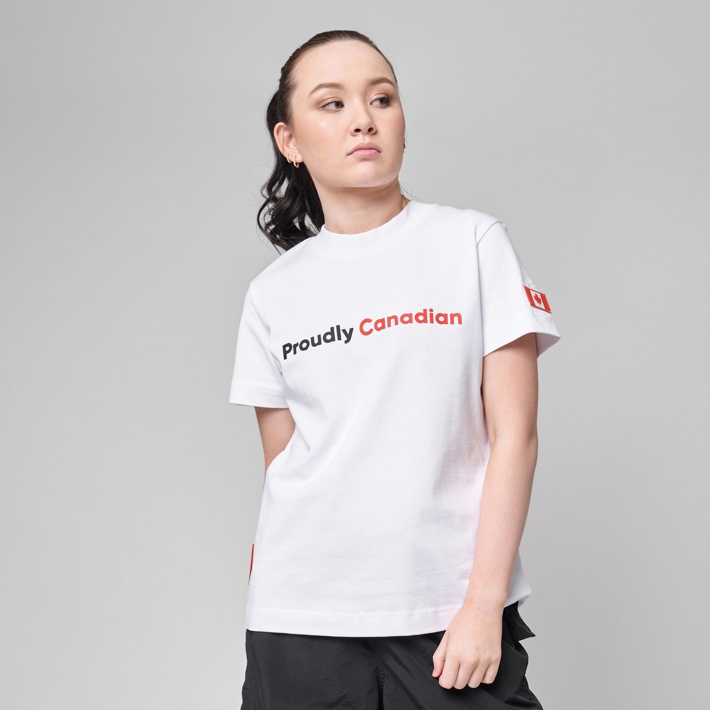 Female model wearing Proudly Canadian Women's T-Shirt in premium white cotton with raised high-density black Proudly and red Canadian typography