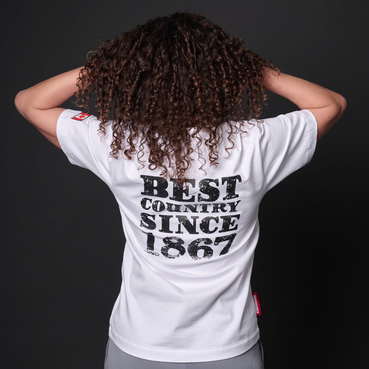 Back view of female model wearing Canada Best Country Since 1867 Unisex T-Shirt showing distressed typography print