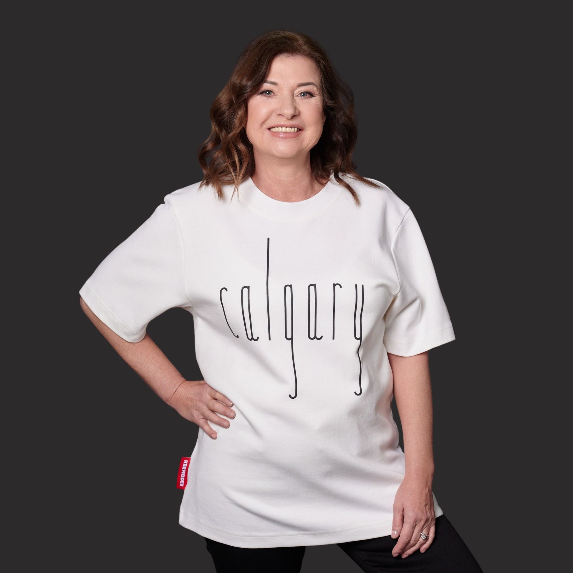 Female model wearing Calgary Alberta Unisex T-Shirt featuring raised high-density Calgary typography and Canadian flag sleeve patch