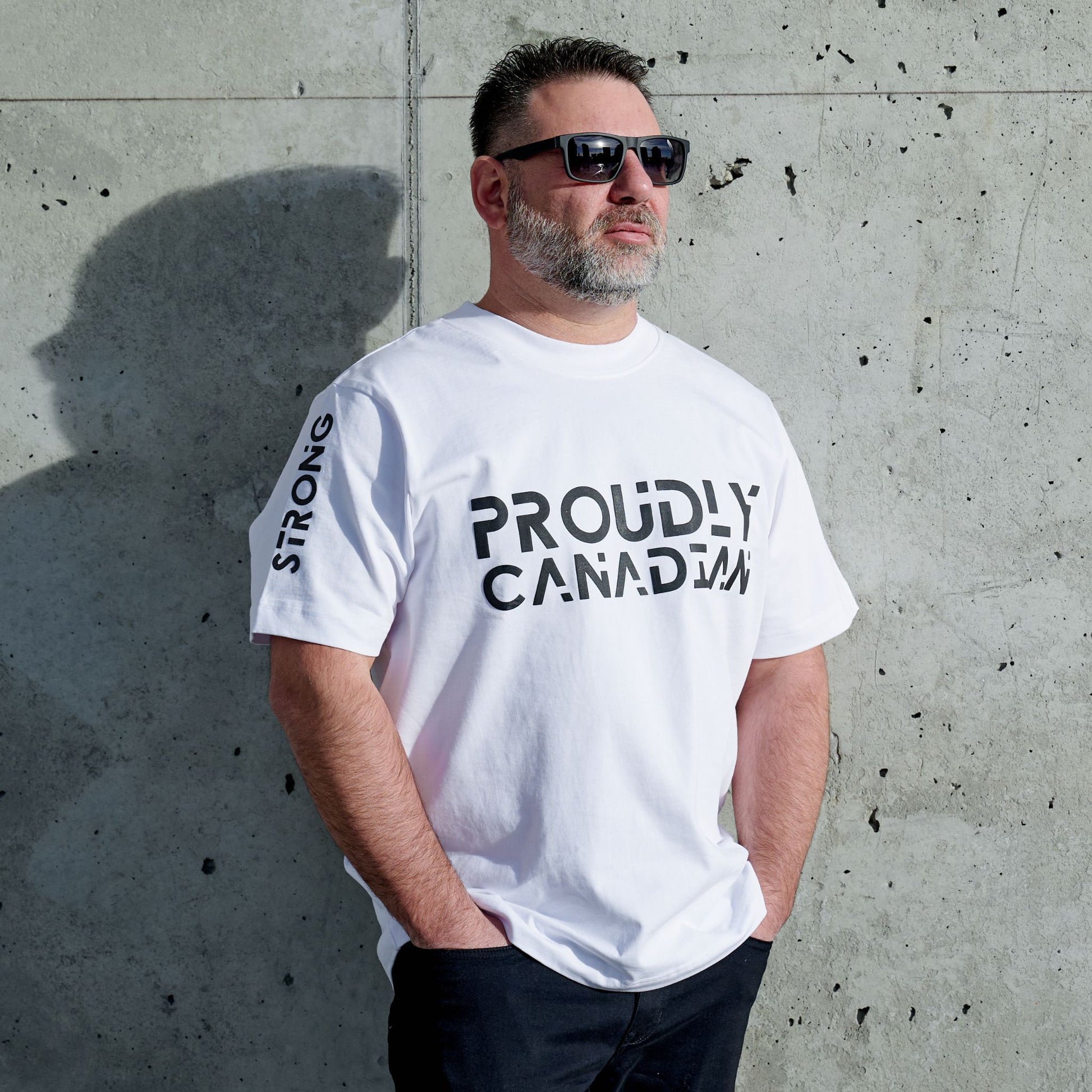 Male model wearing Strong and Free Proudly Canadian Unisex T-Shirt featuring raised high-density Proudly Canadian typography