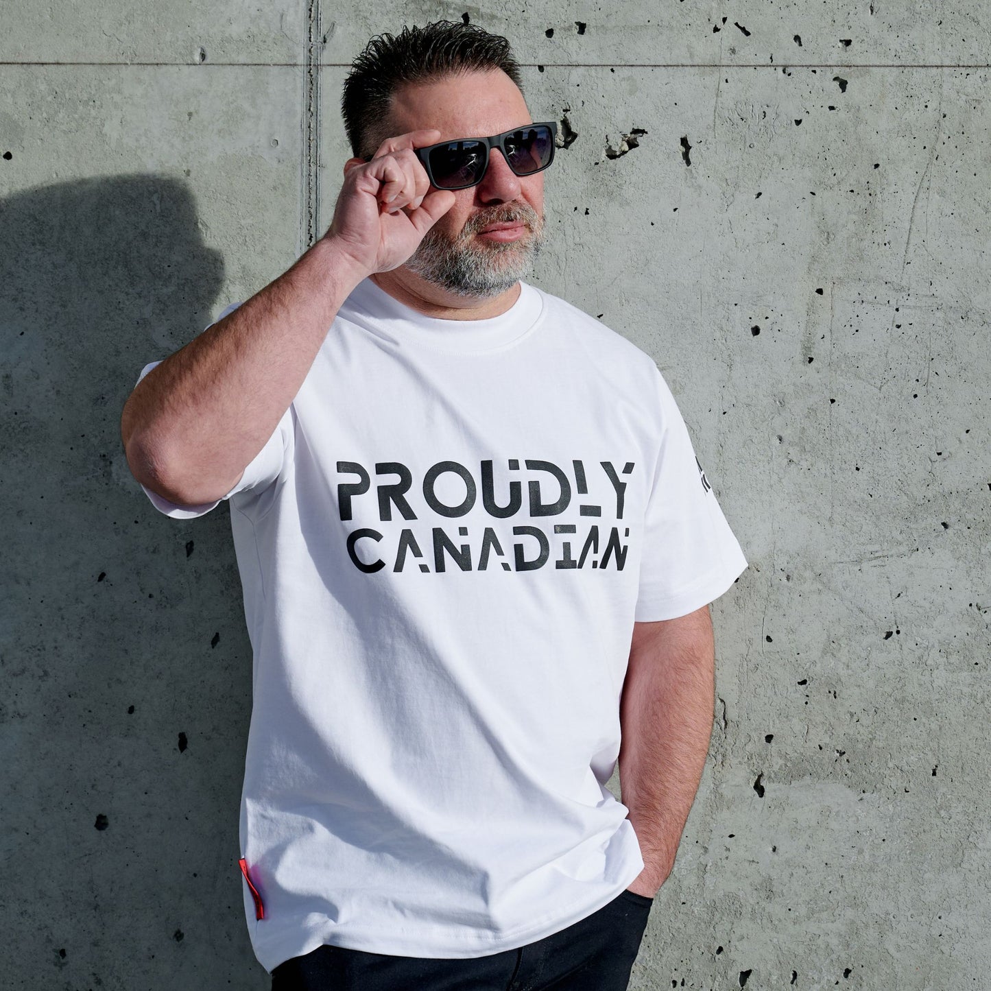 Male model wearing Strong and Free Proudly Canadian Unisex T-Shirt featuring raised high-density Proudly Canadian typography