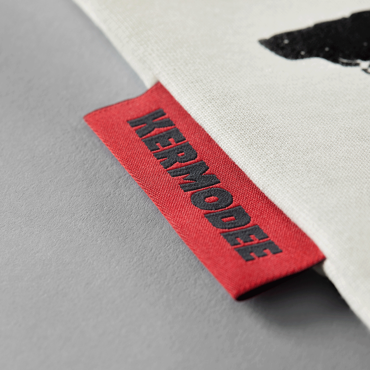 Close-up of red KERMODEE side label on white cream t-shirt right-side seam