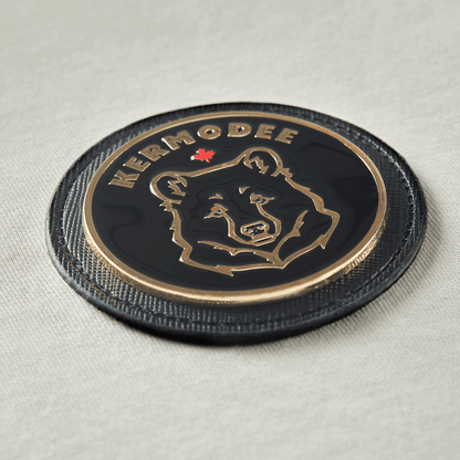 Close-up of circular Kermodee bear emblem with gold contour on cream off-white t-shirt