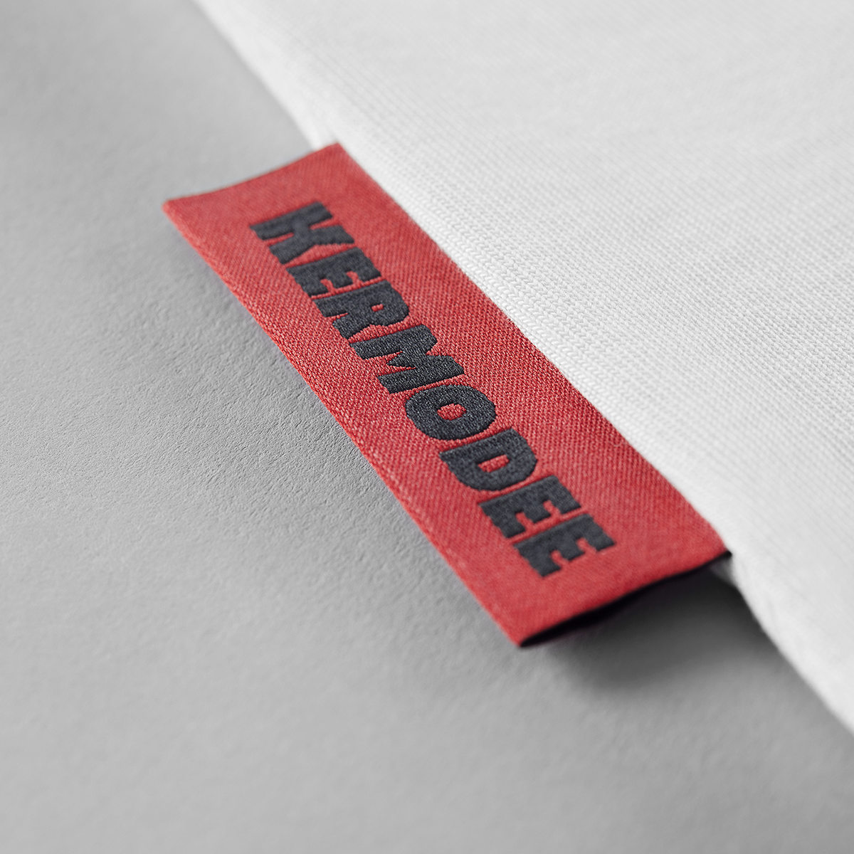 Close-up of red KERMODEE side label on white t-shirt right-side seam