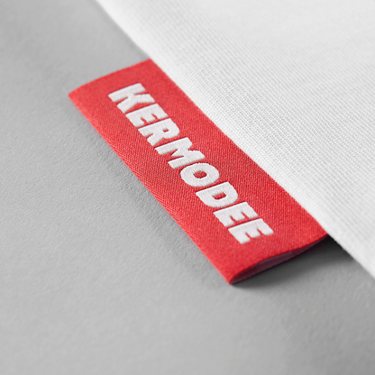 Close-up of red KERMODEE side label on right seam of white t-shirt