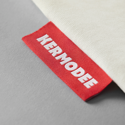 Close-up of red KERMODEE side label on white cream t-shirt right-side seam